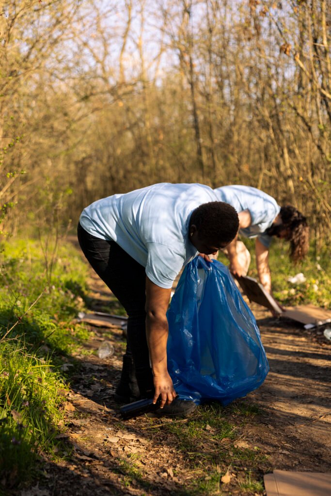 african american woman picking up rubbish and plastic waste from the forest